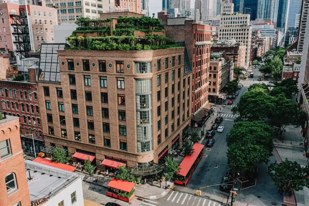 Aerial view of the brick hotel building on a Tribeca corner, with a planted rooftop and red awnings at street level