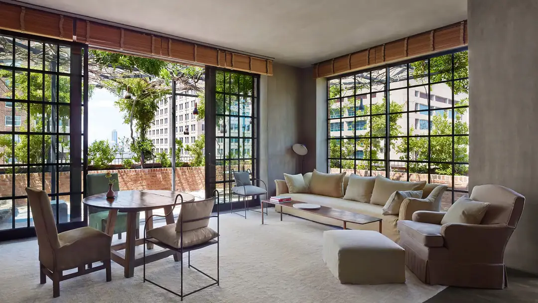 Penthouse living room with linen sofas, a round wood table and steel-framed windows onto a planted roof terrace
