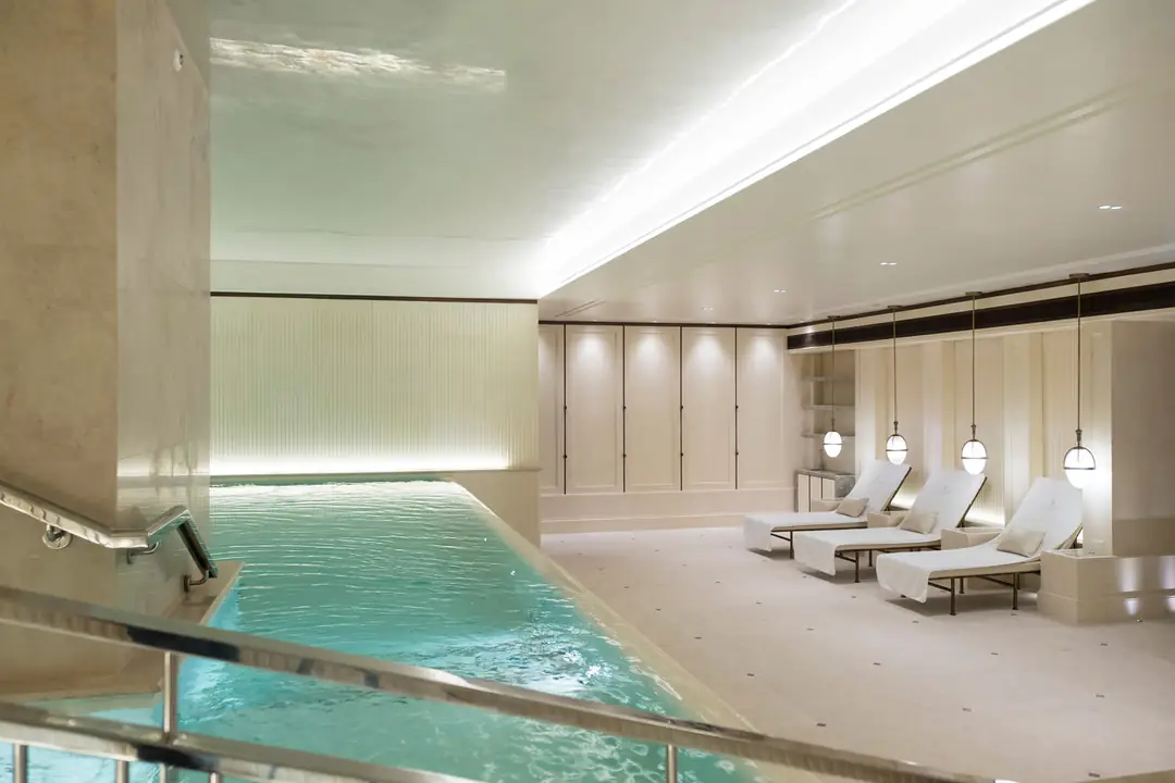 Underground spa pool lined in pale stone, with three white loungers under pendant lamps