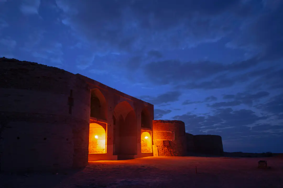 Low earthen arches glowing with lamplight at blue hour