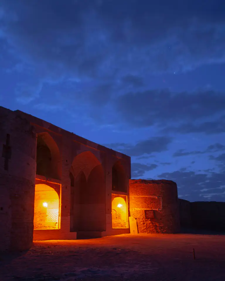 Low earthen arches glowing with lamplight at blue hour